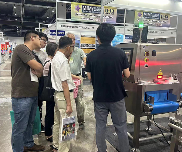 Close-up of visitors examining Foodman inspection equipment specifications, test samples, and performance data