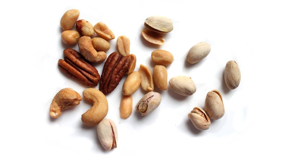 Assorted bulk nuts including almonds, walnuts, peanuts, and hazelnuts on a conveyor for X-ray inspection